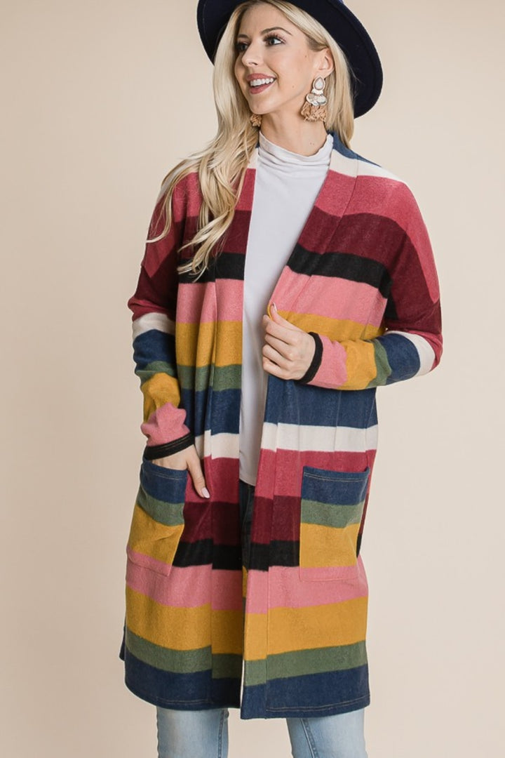 A person wearing a wide-brimmed hat, large earrings, and the BOMBOM Color Block Striped Open Front Cardigan in red, pink, navy, yellow, and white is smiling and posing against a plain background.