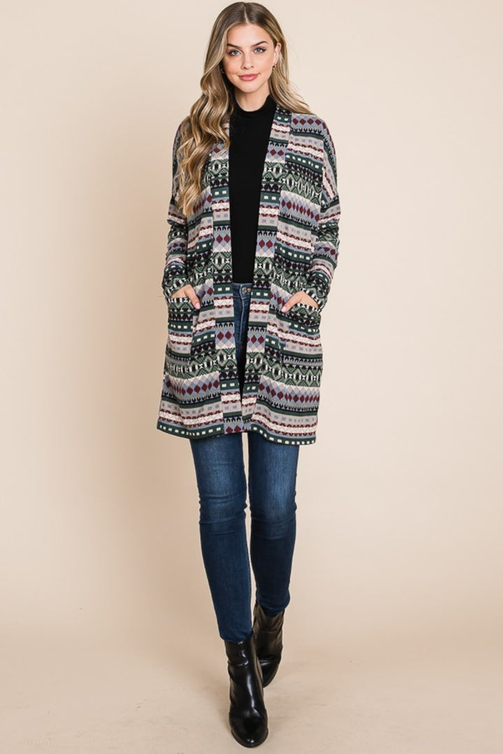 A person with long hair wears the BOMBOM Geometric Open Front Long Sleeve Cardigan with Pockets over a black top and blue jeans against a plain background, hands in pockets, and black ankle boots, presenting an effortlessly stylish look.