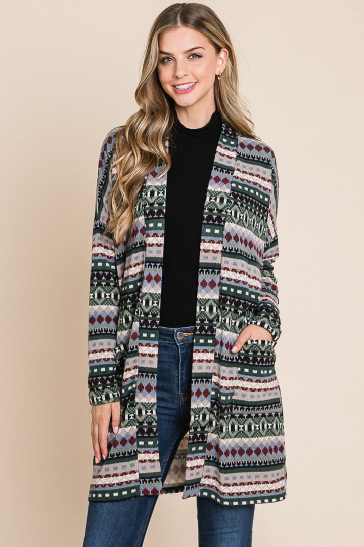 A person wearing the BOMBOM Geometric Open Front Long Sleeve Cardigan with Pockets stands against a plain background, smiling with long hair and their hands in the cardigan pockets. They pair it with a black top and jeans.