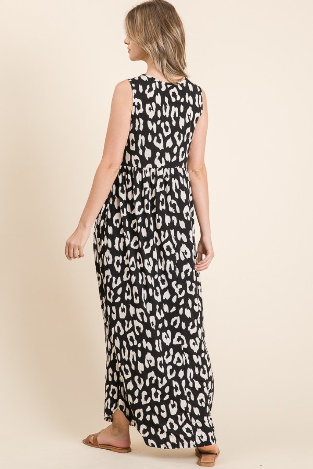 A woman with blonde hair is wearing the BOMBOM Leopard Maxi Dress with Pockets, featuring waist shirring for a flattering fit. She stands sideways, looking left against a plain light beige background.