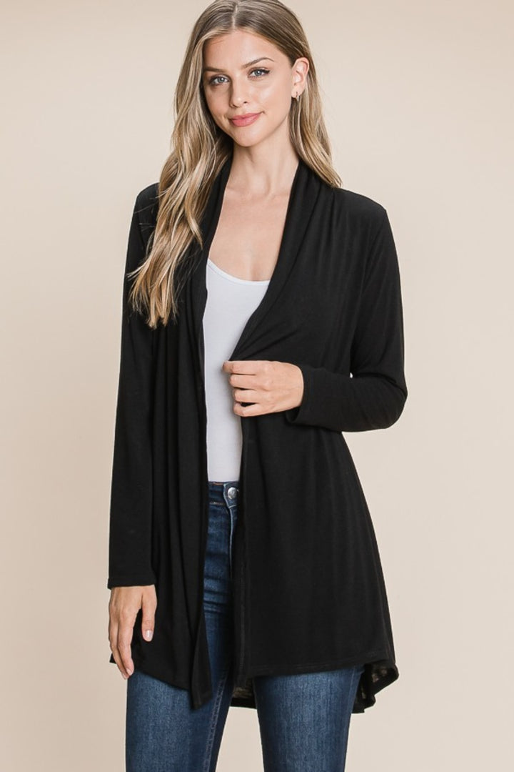 Against a beige background, a woman wears the BOMBOM Open Front Long Sleeve Cardigan in chic black, made of soft knit. It elegantly layers over her white top and blue jeans.