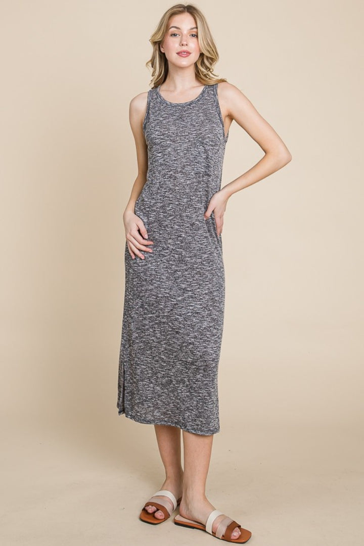 A woman exudes chic elegance in a BOMBOM Round Neck Slit Midi Tank Dress, posing against a beige background. The sleeveless gray dress enhances her summer look, perfectly complemented by her brown and white sandals. She stands confidently with her left hand on her hip, slightly smiling.