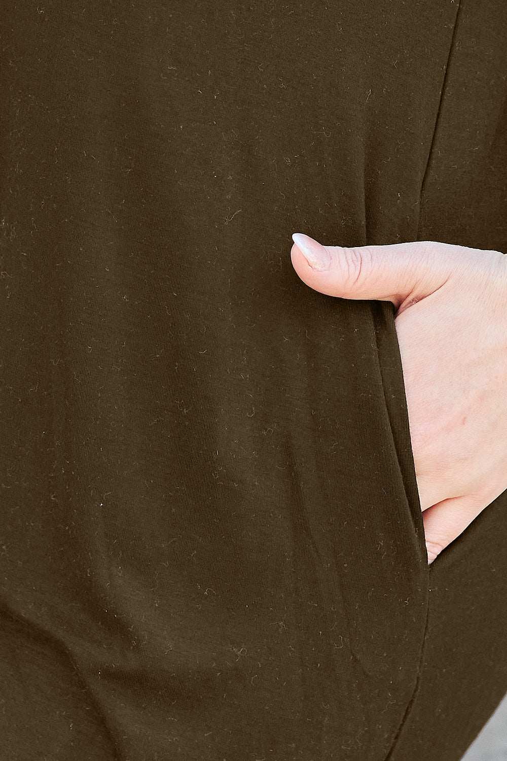 A close-up of a person’s hand resting inside the pocket of a Basic Bae Full Size Round Neck Short Sleeve Dress, crafted from a soft spandex blend and featuring textured dark fabric. The skin tone of the hand is light, and the dress is machine wash cold friendly.