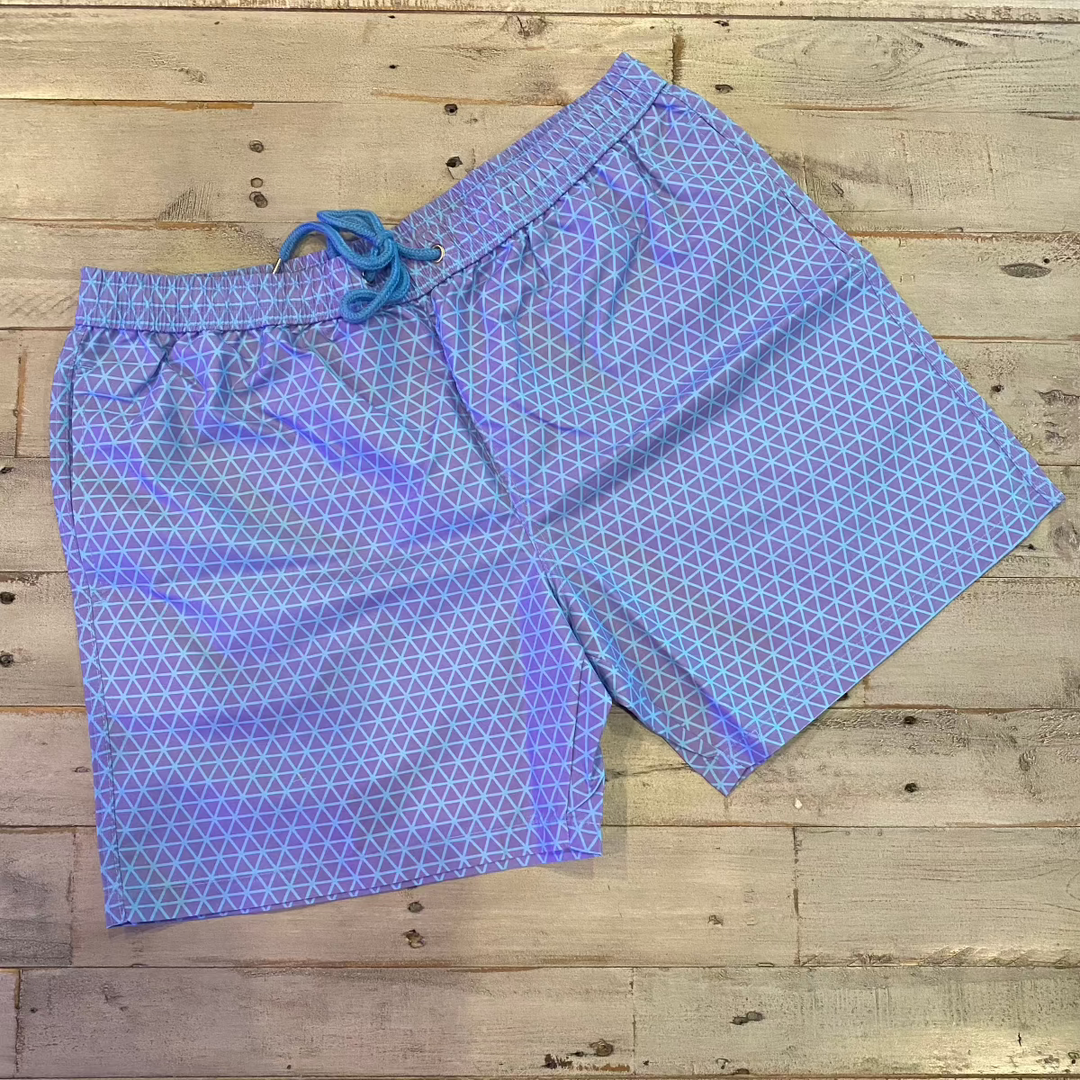 Laid flat on a wooden surface, the Geo Pattern Men Color Changing Trunks boast an eye-catching blue and white geo design. The drawstring waist offers a comfortable fit, while the unique color-changing fabric brings an exciting element to your summer attire.