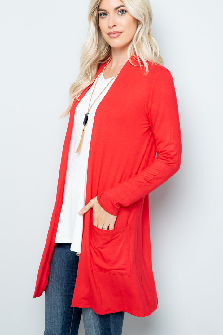 A person with long blonde hair wears the Celeste Full Size Open Front Cardigan with Pockets in red over a white top and blue jeans, accessorized with a long necklace, against a light gray background. This versatile layering piece effortlessly enhances their outfit.