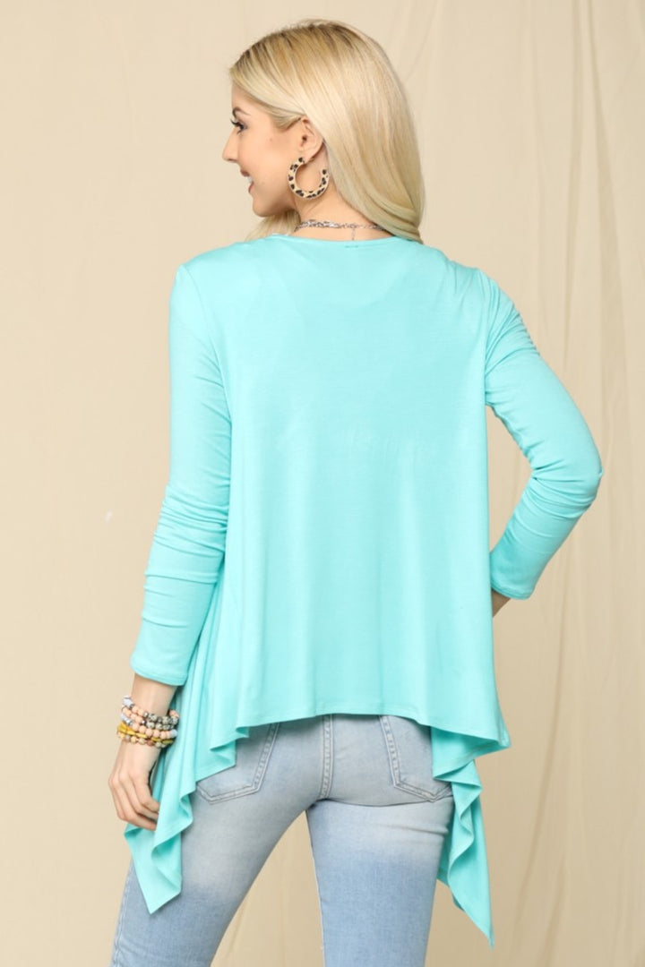 A person with long hair, in a turquoise asymmetric top and light blue jeans, faces away from the camera. Theyre styled with hoop earrings, beaded bracelets, and the Celeste Full Size Open Front Knit Cardigan. The background is neutral.