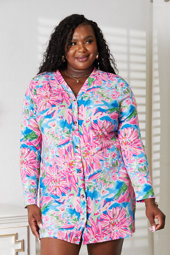 In a brightly lit room, a woman beams in a Double Take Floral Open Front Long Sleeve Cardigan with shades of pink, blue, and green. Her long curly hair and subtle jewelry complete the romantic and elegant vibe as light filters through the window, casting soft shadows on the wall behind her.