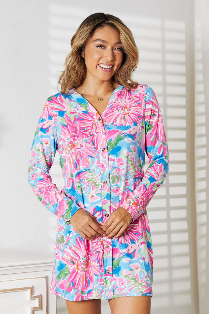 A woman exudes feminine charm in a Double Take Floral Open Front Long Sleeve Cardigan, its vibrant pink, blue, and green hues enhancing her romantic and elegant look. She stands gracefully in a well-lit room, with window-cast shadows dancing on the wall.