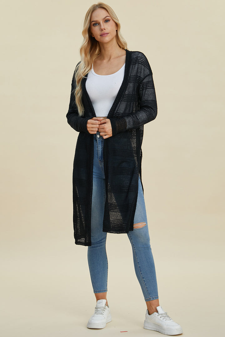 A person with long blonde hair wears the Double Take Full Size Open Front Longline Cardigan in black over a white top and ripped blue jeans, showcasing the delicate stretch of the knit. They're standing with hands clasped against a neutral background, completing the look with white sneakers that add to their casual elegance.