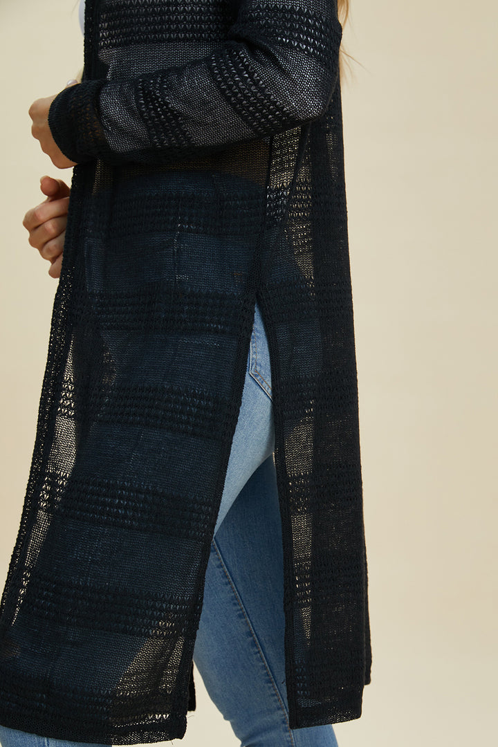 A close-up shows someone wearing the Double Take Full Size Open Front Longline Cardigan, featuring black openwork detailing and side slits, paired with light blue jeans. The backdrop is a soft beige.