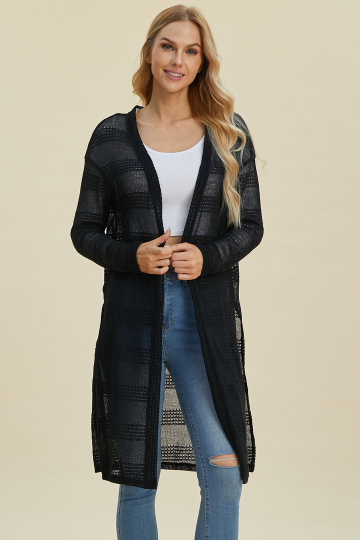 A woman with long blonde hair wears the Double Take Full Size Open Front Longline Cardigan in black, crafted from stretch polyester, over a white top and blue jeans. She is standing against a plain background, smiling at the camera.