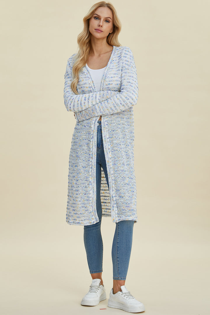 A person wearing the Double Take Full Size Open Front Longline Cardigan, featuring a blue and white pattern, pairs it with a white top, stretch blue jeans, and white sneakers. They stand against a plain background with long, wavy blonde hair and maintain a neutral expression.