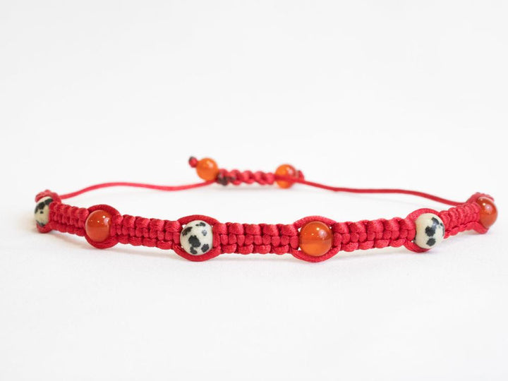 Introducing the Gem and Stone Beach Bracelets by Claire: a unique, handcrafted red macrame bracelet featuring an exquisite arrangement of alternating patterned and solid beads. This distinctive gemstone bracelet pops beautifully against a white background.