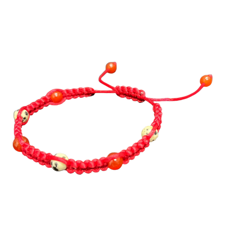 The "Gem and Stone Beach Bracelet by Claire" in a vibrant red hue is showcased on a black textured surface. This handcrafted accessory flaunts small, round beads and an adjustable closure with dual strings, making it a notable item among gemstone accessories.