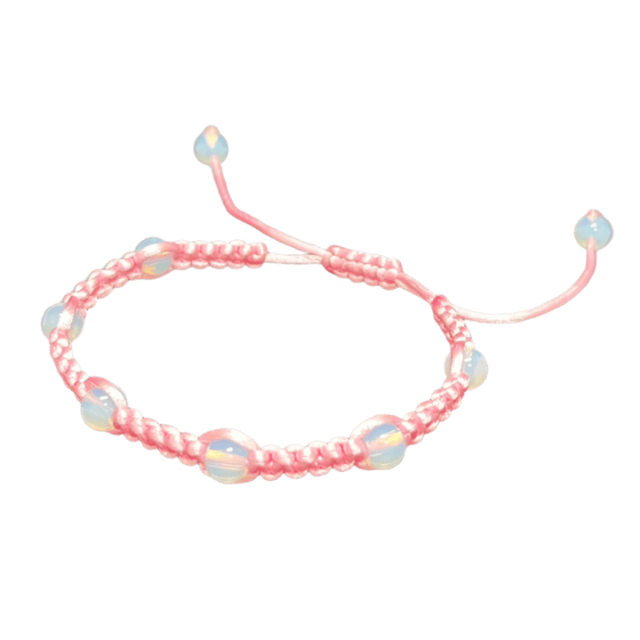 The Gem and Stone Beach Bracelets by Claire shimmer elegantly with pink braiding and blue iridescent beads, contrasting beautifully against a dark fabric background. This handcrafted piece features adjustable ends adorned with beads, making it an ideal choice for beachwear enthusiasts looking for a stylish gemstone touch.