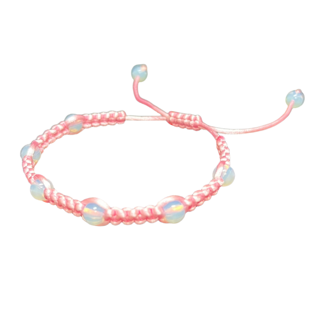 The Gem and Stone Beach Bracelets by Claire are handcrafted pink woven accessories featuring adjustable ends and opalescent beads, beautifully displayed on a plain black background to capture the essence of unique beachwear.