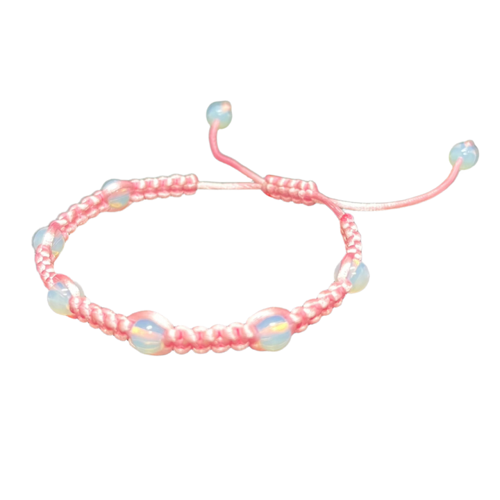 The Gem and Stone Beach Bracelets by Claire are handcrafted pink woven accessories featuring adjustable ends and opalescent beads, beautifully displayed on a plain black background to capture the essence of unique beachwear.