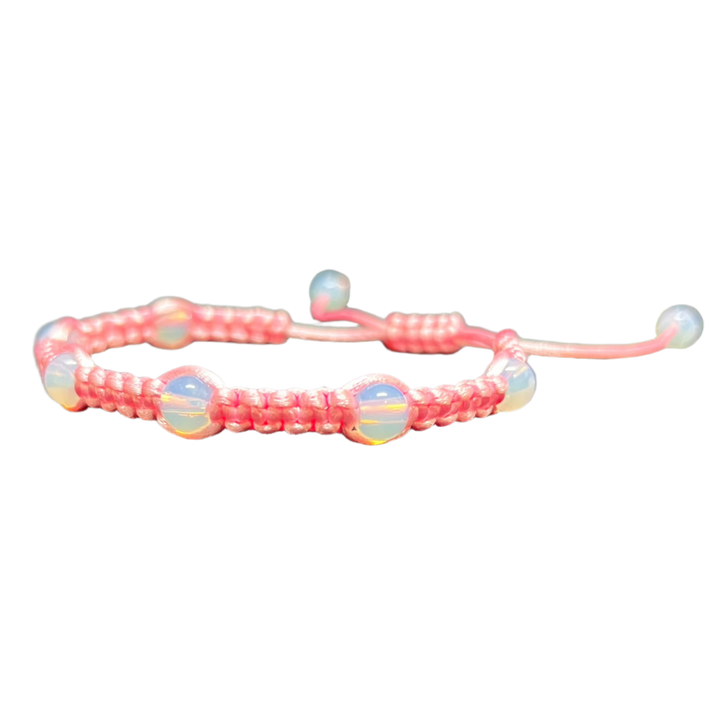 The Gem and Stone Beach Bracelet by Claire, featuring a pink woven design adorned with iridescent beads, is displayed against a black backdrop. This handcrafted piece highlights an adjustable closure, making it a standout in gemstone accessories.