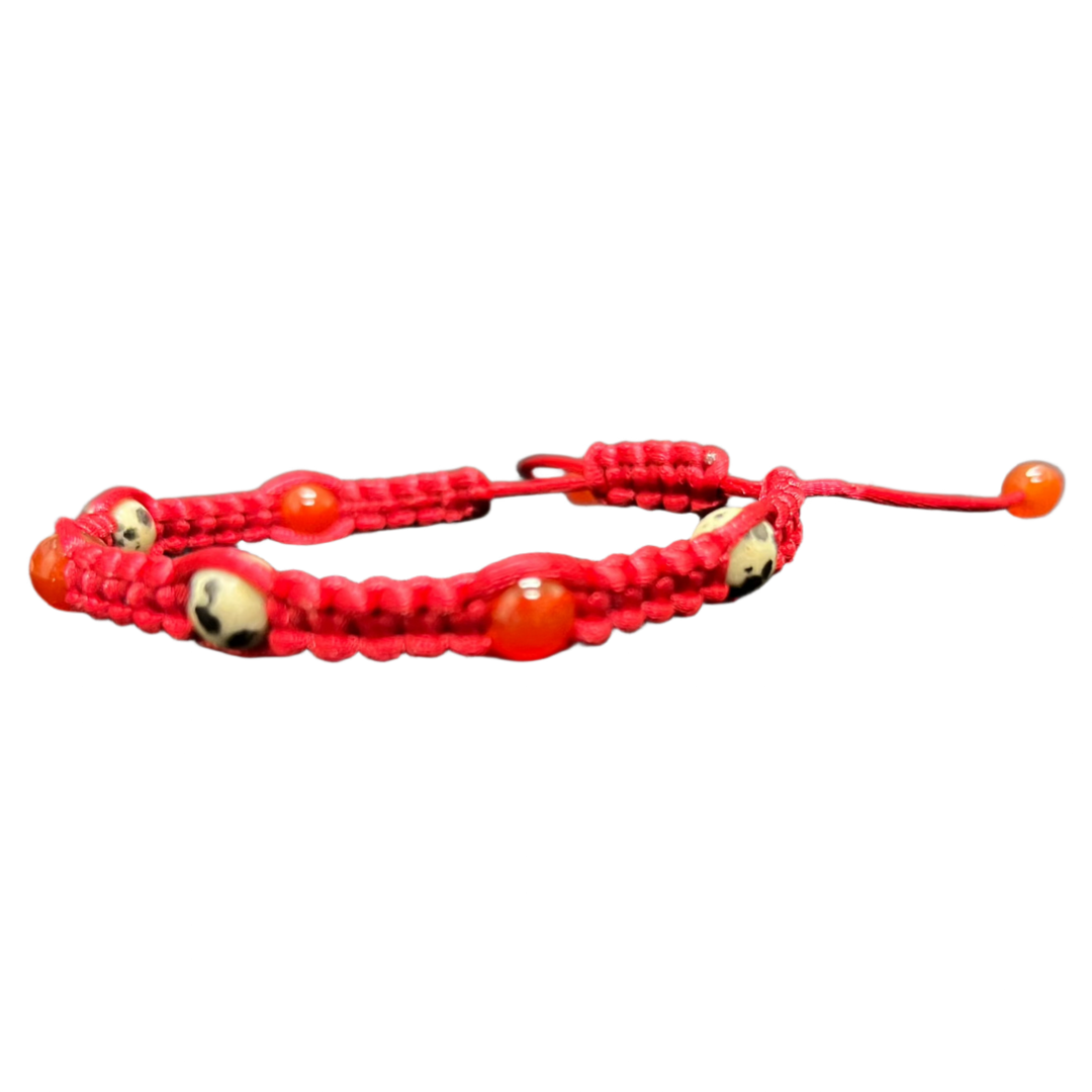 The Gem and Stone Beach Bracelets by Claire, showcasing red braided cord with small round red and beige beads, are beautifully displayed on a dark textured surface, adding a distinctive flair to your beach wear collection.