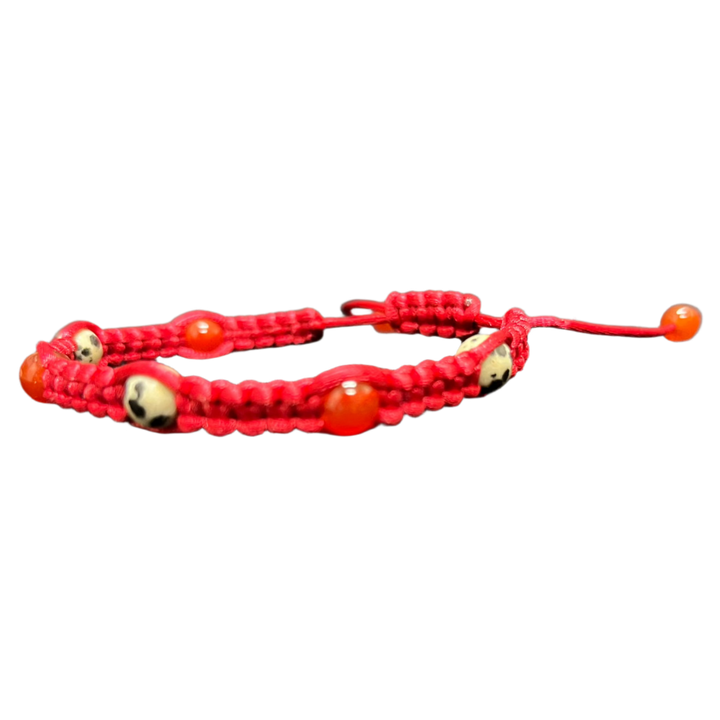 The Gem and Stone Beach Bracelets by Claire, showcasing red braided cord with small round red and beige beads, are beautifully displayed on a dark textured surface, adding a distinctive flair to your beach wear collection.