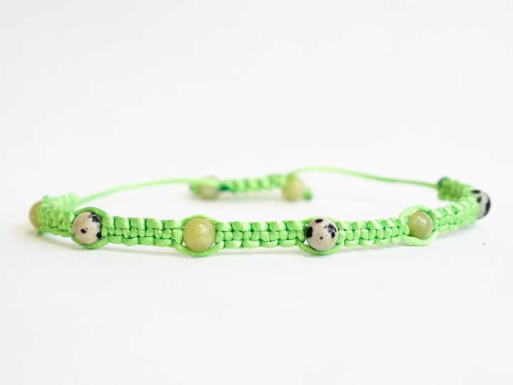 Introducing the Gem and Stone Beach Bracelets by Claire: A unique bracelet that boasts a green macramé cord adorned with round, spotted beads. Its adjustable closure ensures a perfect fit for any wrist. Set against a plain white background, the vibrant colors of this standout accessory truly shine.