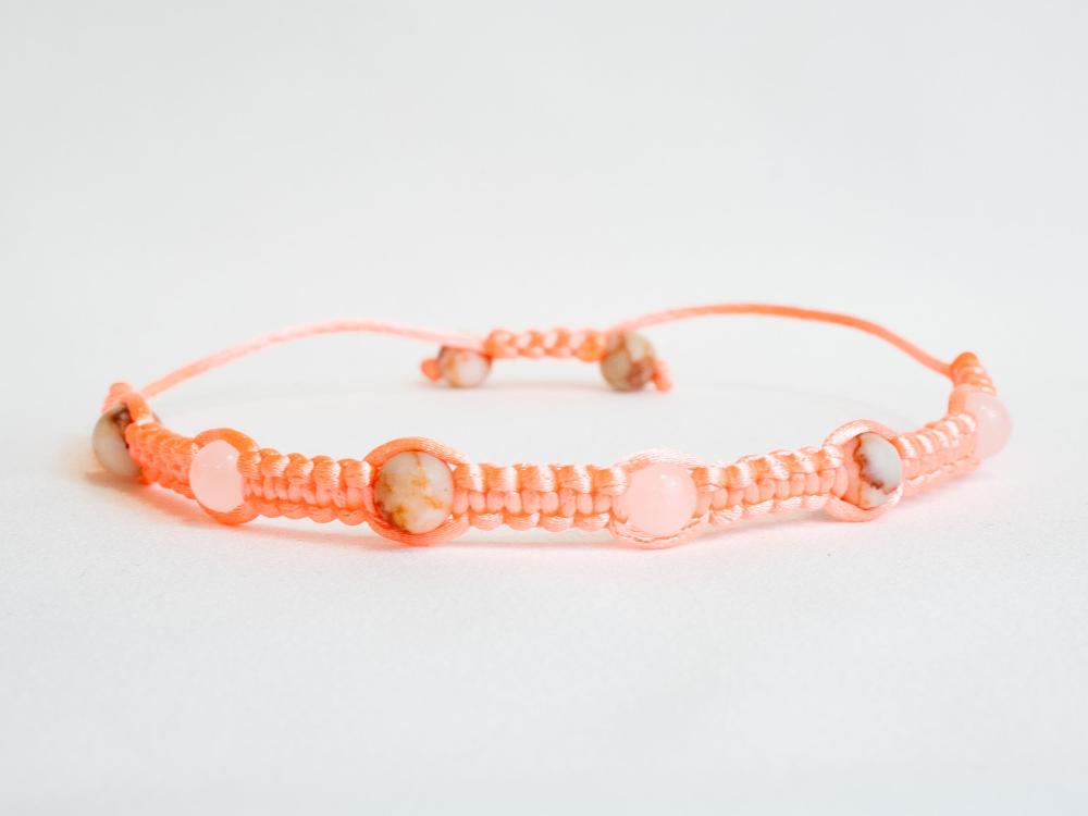 The Gem and Stone Beach Bracelet by Claire is a unique piece, featuring a handmade friendship design with a pink woven cord and pink marbled beads, beautifully showcased against a plain white background.