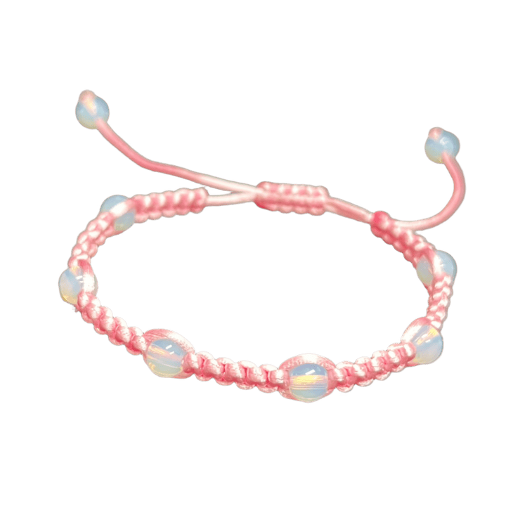 A unique, pink braided "Gem and Stone Beach Bracelet by Claire," featuring iridescent beads, rests on a black surface. The adjustable strings are extended behind it, creating a simple, elegant display.