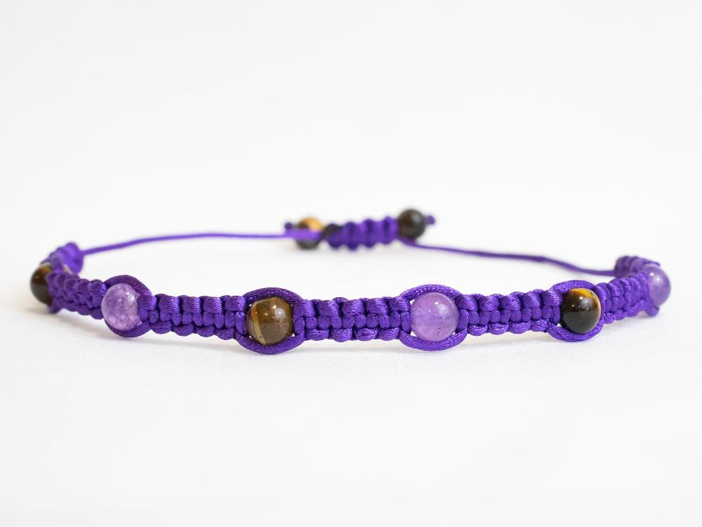 The "Gem and Stone Beach Bracelets by Claire" showcases a distinctive macramé bracelet in purple, adorned with round beads made from unique gemstones in charming shades of purple and brown, elegantly displayed on a white background.