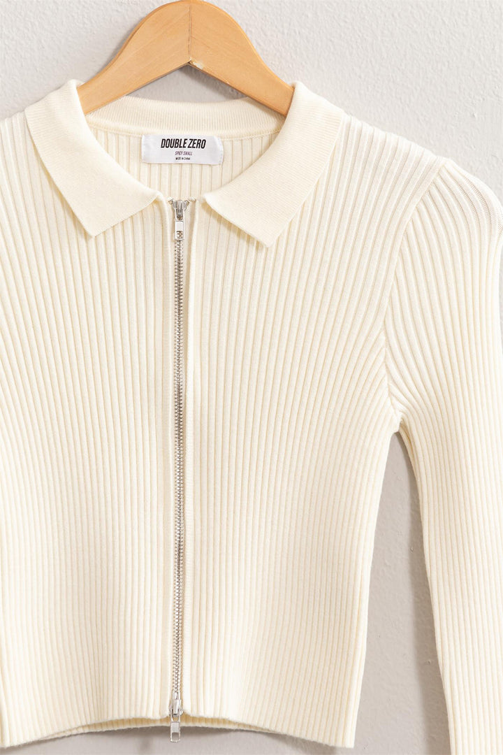 The HYFVE Ribbed Double Zip Cropped Cardigan, displayed on a wooden hanger against a light wall, effortlessly embodies the charm with its cream-colored ribbed texture and elegant collar design.