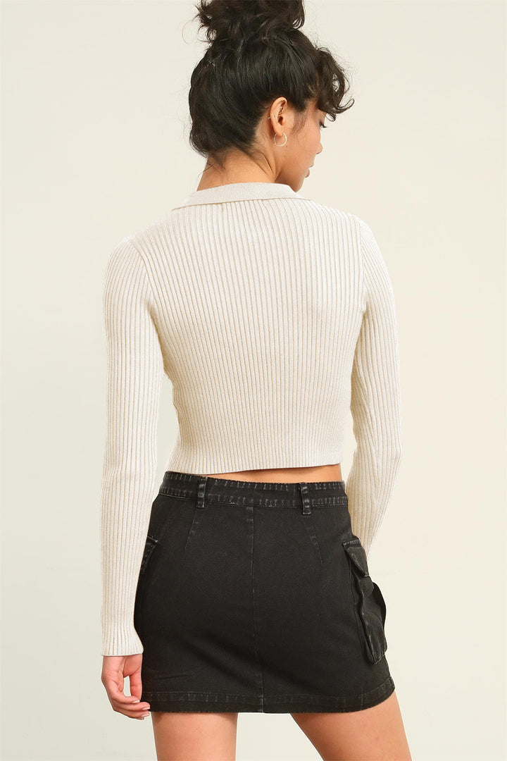 A person with dark hair in a bun stands with their back to the camera against a plain light background, wearing a versatile garment—a HYFVE Ribbed Double Zip Cropped Cardigan in white—and a black denim mini skirt with pockets.