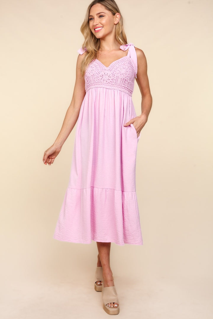 A woman in a Haptics Crochet Lace Ruffle Hem Cami Midi Dress, light pink with a chic babydoll silhouette, stands against a neutral background. She smiles, wearing beige platform sandals, with her left hand in the dress pocket.