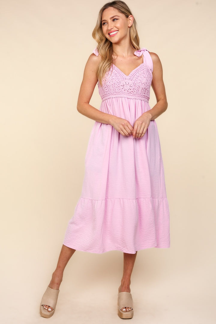 A woman in a pink Haptics Crochet Lace Ruffle Hem Cami Midi Dress with a V-neck is smiling against a neutral background. Her long, light hair cascades as she confidently stands in her wedge sandals.