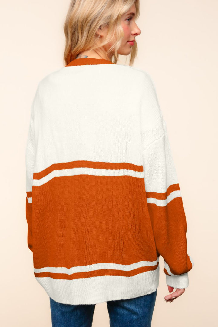 A person with long blonde hair is shown from the back, wearing a Haptics Full Size V Neck Button Down Letter Patch Cardigan in an oversized white and orange stripe design, against a neutral beige background.