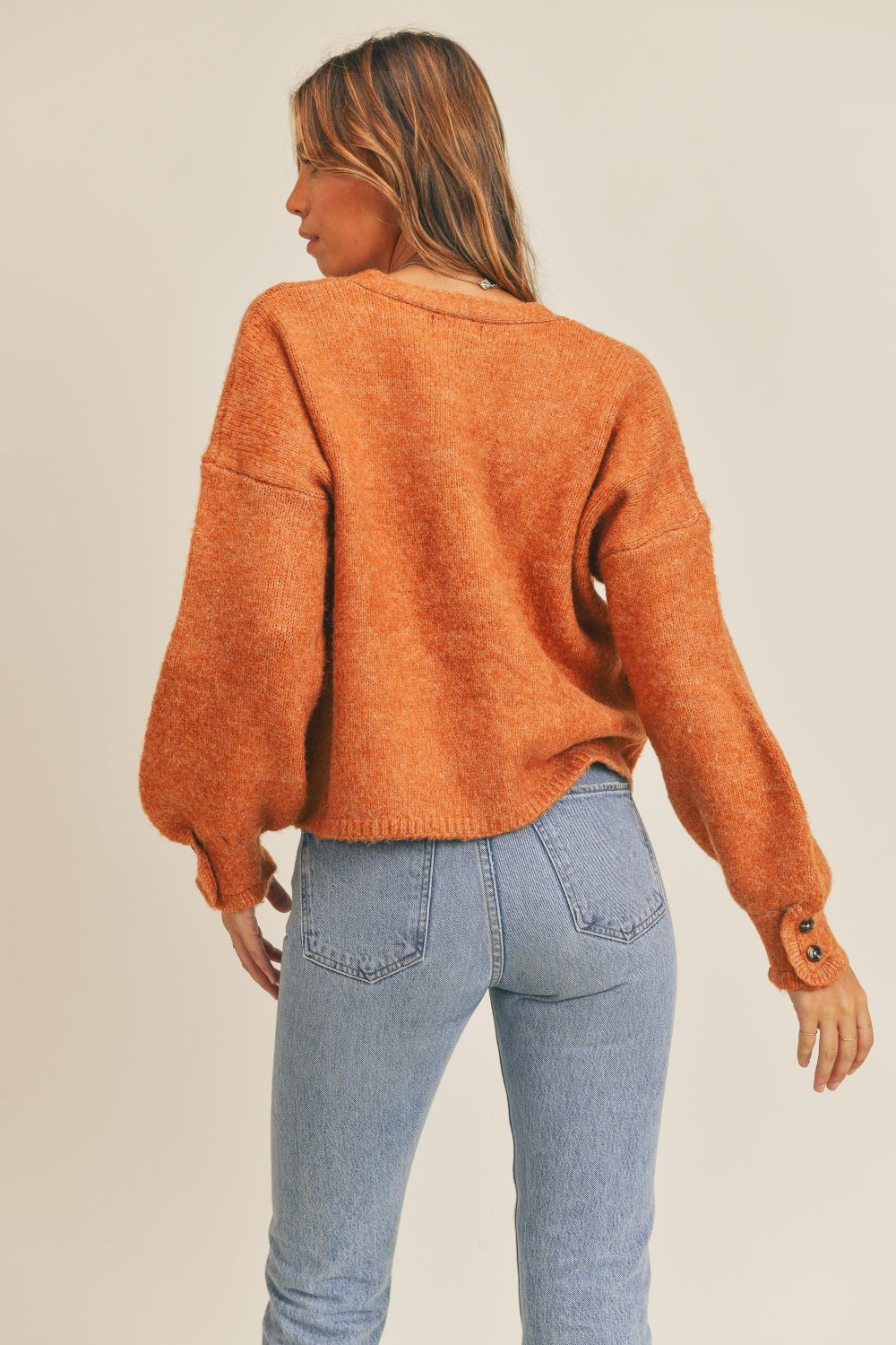 A person with long hair is seen from the back wearing a vibrant MABLE Long Sleeve Button Down Sweater Cardigan made of soft knit fabric and light blue jeans, set against a plain background.