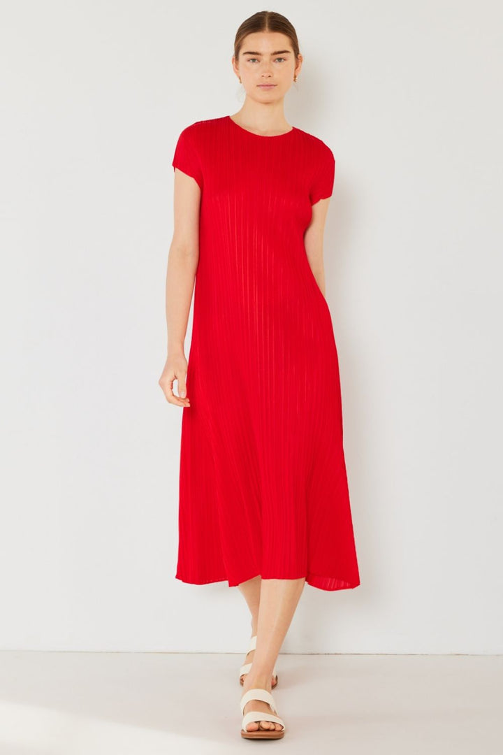 Against a white backdrop, a person exudes feminine charm in the red Marina West Swim Pleated Cap Sleeve A-Line Dress. Paired with white sandals and hair tied back, their relaxed posture adds to the effortless elegance.