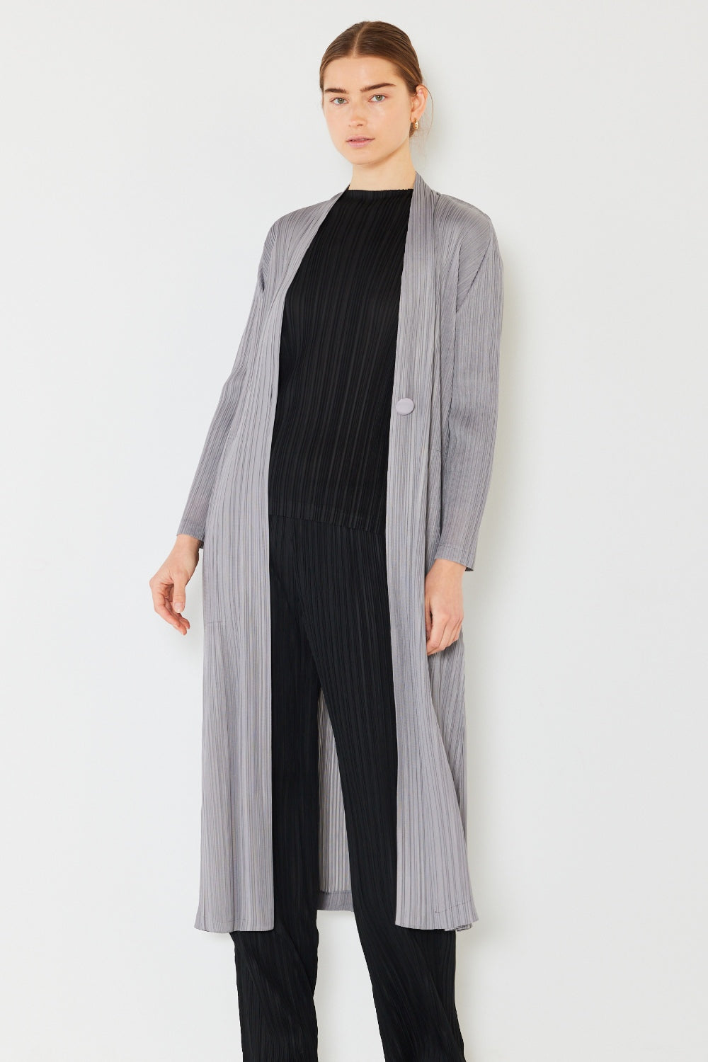 A person is wearing a stylish Marina West Swim Pleated Long Sleeve Cardigan over a black, pleated top and pants. This versatile layering piece stands out as they pose against a plain white background.