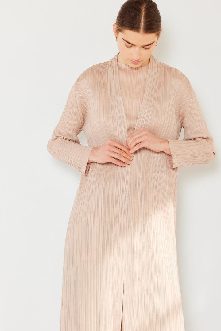 A person with dark hair is wearing the Marina West Swim Pleated Long Sleeve Cardigan in beige. They are looking down, fastening the front of this versatile layering piece against a plain white background.