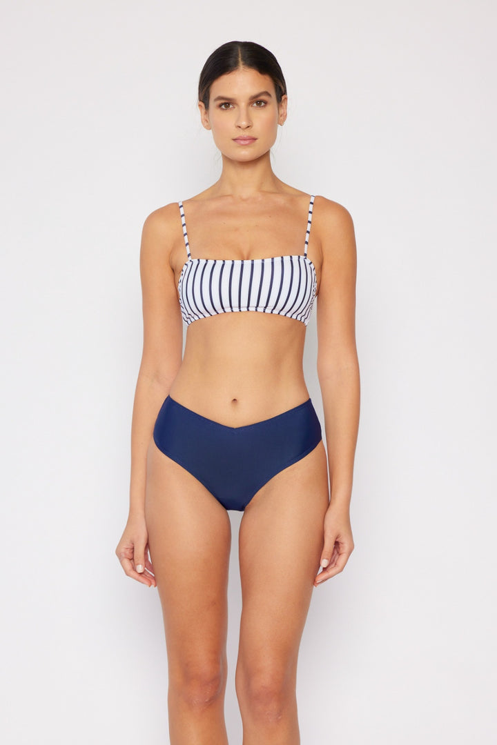 Wearing the Marina West Swim Striped Bikini Set, a person stands against a plain background. The bandeau top has white with black vertical stripes and removable bra pads, while the navy blue bottoms are solid. They face forward with a neutral expression.