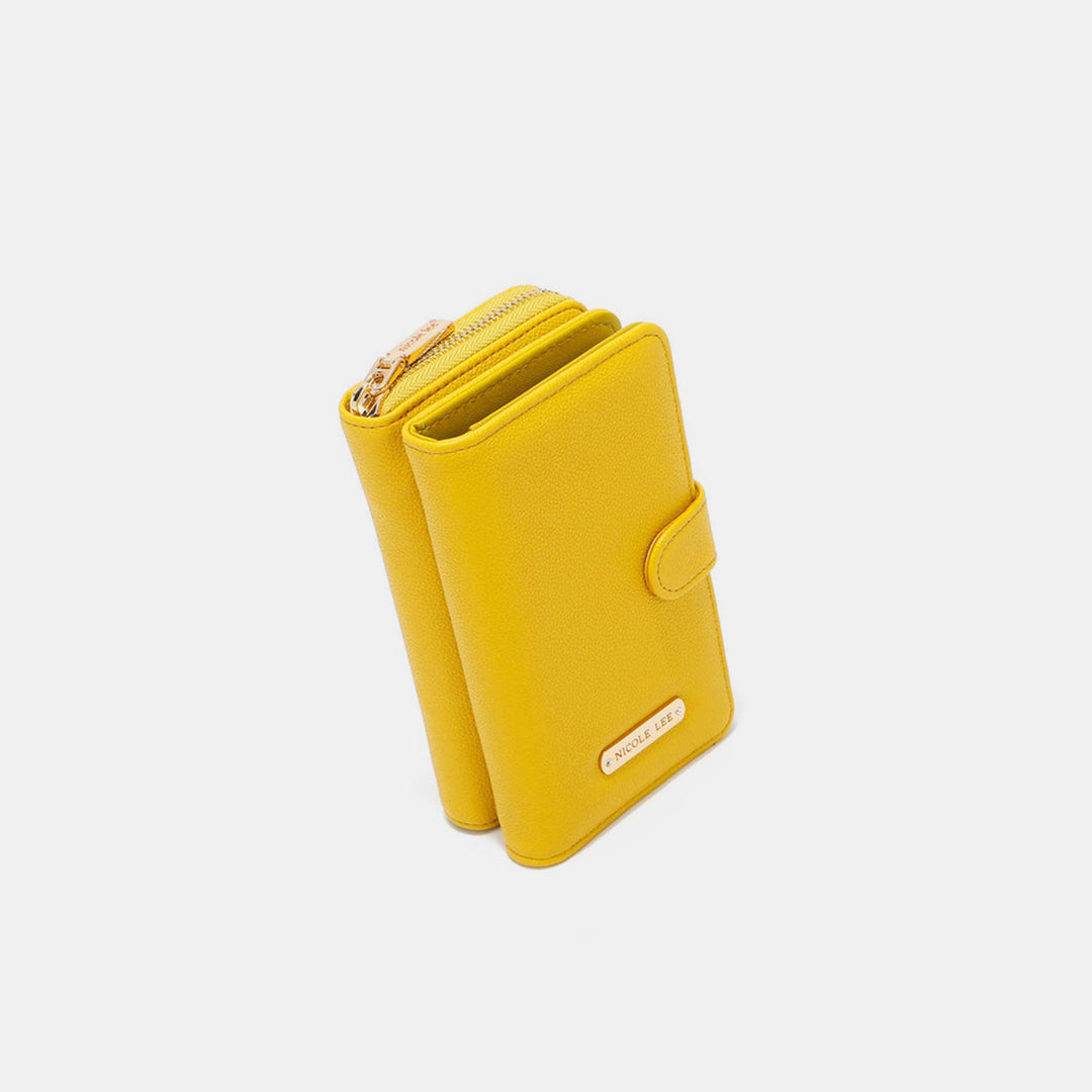 The Nicole Lee USA 2 Piece Phone Case Crossbody Wallet is yellow and made from vegan leather, featuring a strap, snap closure with a gold logo plate, and an upper zippered compartment. It resembles an elegant phone case and is set against a plain white background.