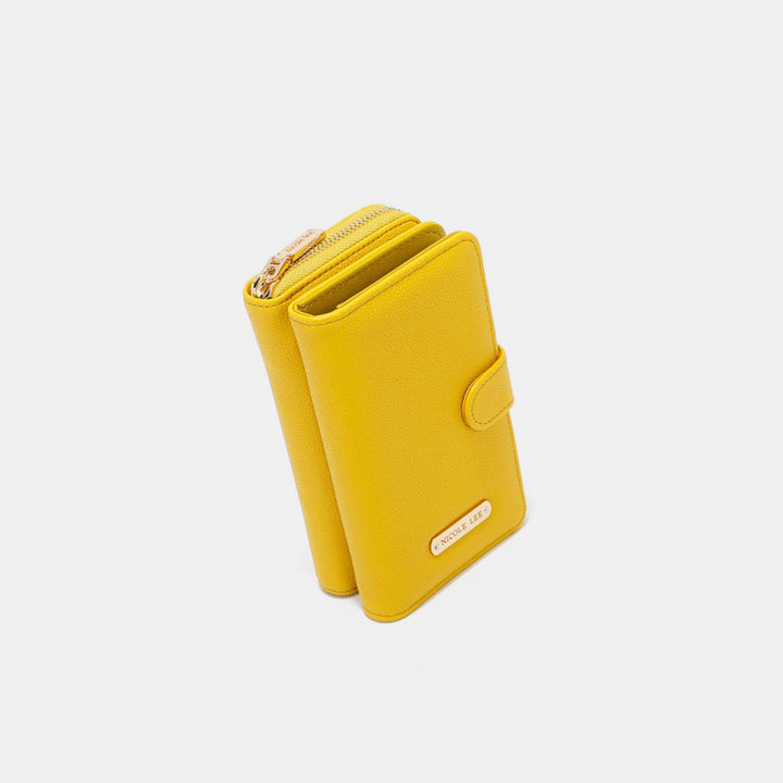 The Nicole Lee USA 2 Piece Phone Case Crossbody Wallet is yellow and made from vegan leather, featuring a strap, snap closure with a gold logo plate, and an upper zippered compartment. It resembles an elegant phone case and is set against a plain white background.