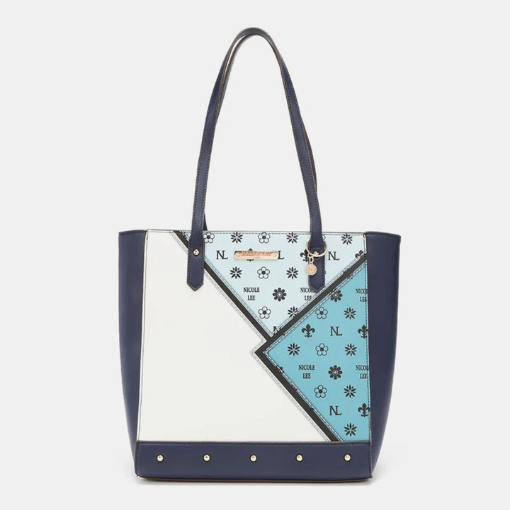 The Nicole Lee USA 3-Piece Color Block Handbag Set showcases a geometric design with navy, white, and light blue vegan leather panels, floral patterns, NOOKER LEE text on the light blue section, dark blue handles, and gold accents.