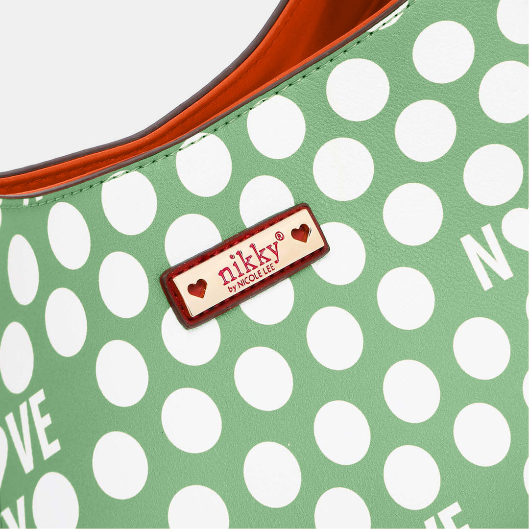 Close-up of a green contrast polka dot handbag made from vegan leather, with an orange interior. A small nikky by NICOLE LEE label is adorned with hearts. Partial white letters on the green background add charm to the Nicole Lee USA Contrast Polka Dot Handbag.