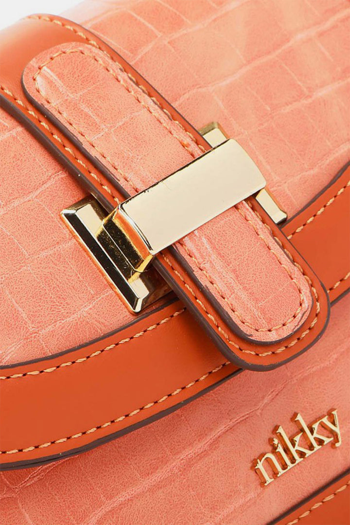 A close-up of the chic Nicole Lee USA Croc Embossed Crossbody Bag reveals its textured orange finish. This stylish accessory boasts gold hardware and a clasp, with "nikky" elegantly displayed in gold near the bottom. The neat stitching highlights the eco-leather craftsmanship.