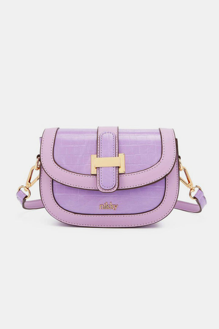 The Nicole Lee USA Croc Embossed Crossbody Bag is a small, stylish accessory in a lilac hue, crafted from eco-leather and featuring a textured surface with gold accents. It includes a flap closure with a gold buckle and an adjustable strap, with the brand name embossed prominently on the front.