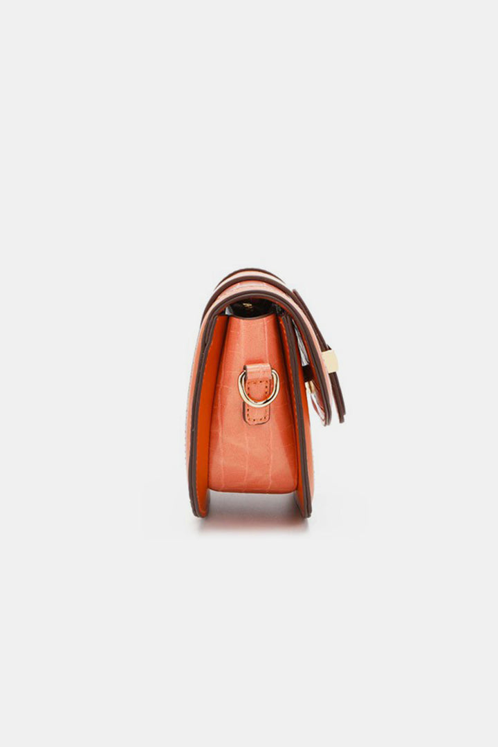 Side view of an orange Nicole Lee USA Croc Embossed Crossbody Bag featuring a brown strap and gold buckle. This stylish accessory showcases a sleek, structured design that highlights its slim profile against a plain background.