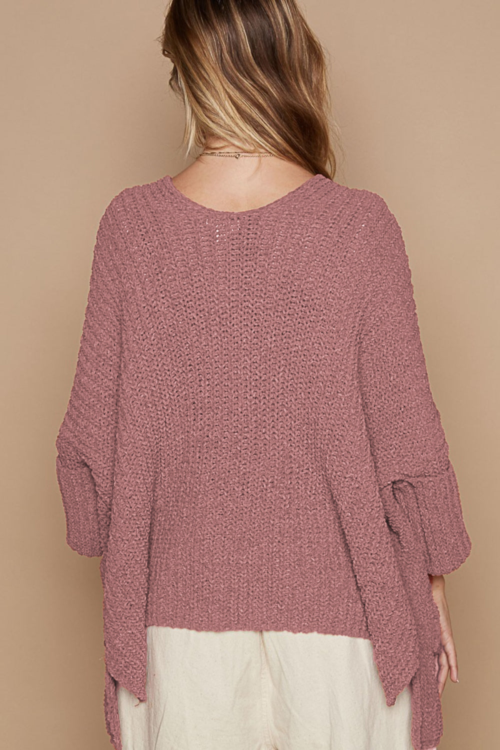 A person with long hair is sporting the POL Open Front Sweater Cardigan with Pockets in a cozy, oversized mauve style. The rolled-up sleeves and ribbed knit pattern enhance its comfortable look. Complemented by a light-colored skirt or pants, they're poised against a beige background.