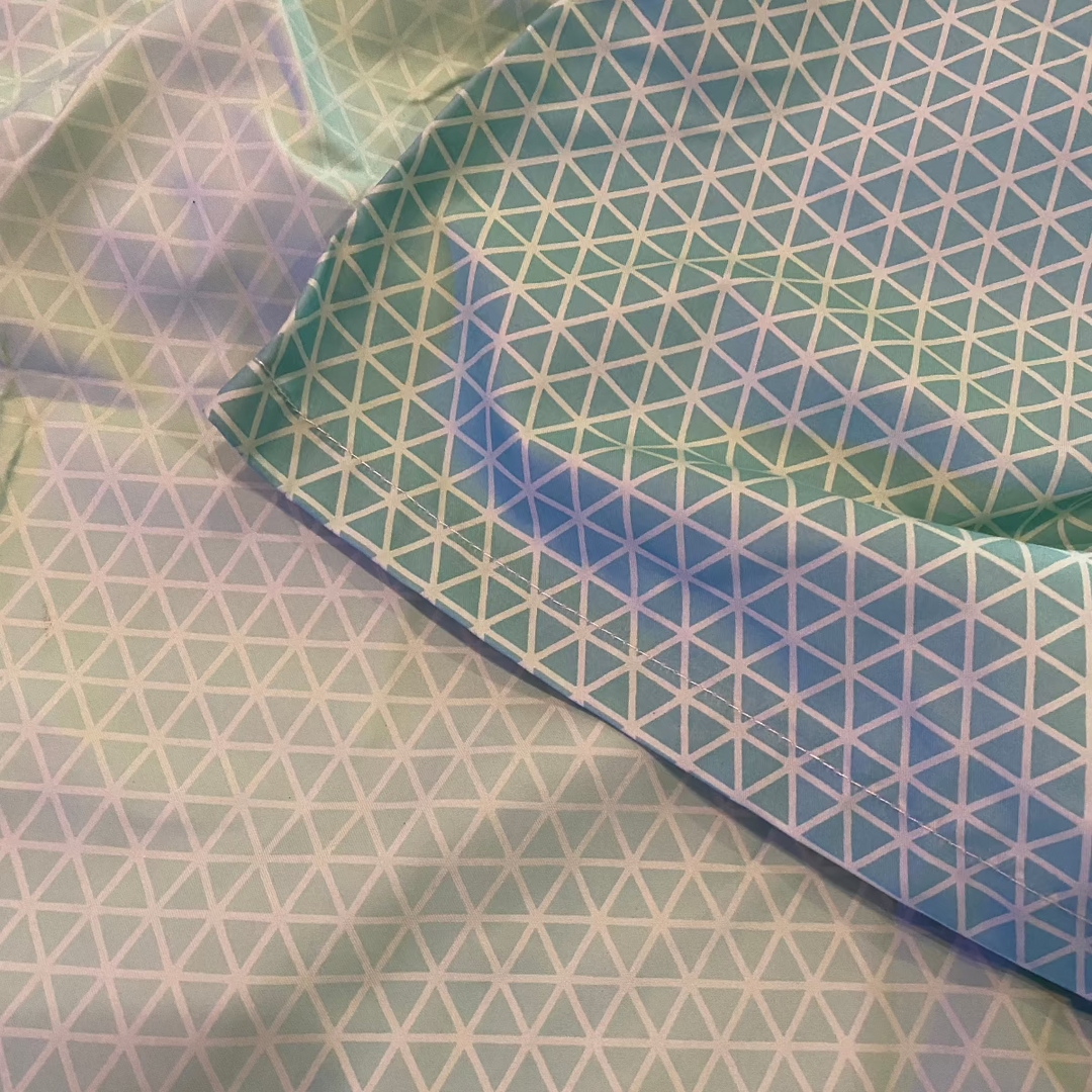 Close-up of a light blue fabric for the Geo Pattern Men Color Changing Trunks, featuring a repeating white triangle geo pattern. The folded fabric creates shadows and highlights, enhancing the geometric design's dynamic appearance.