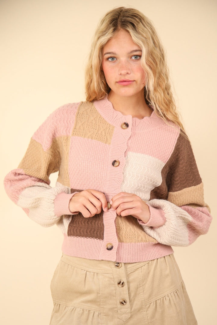 A young woman with long blonde hair is wearing the VERY J Color Block Button Down Textured Sweater Cardigan featuring pink, beige, and brown tones. Against a neutral background, she gazes directly at the camera with a relaxed expression.