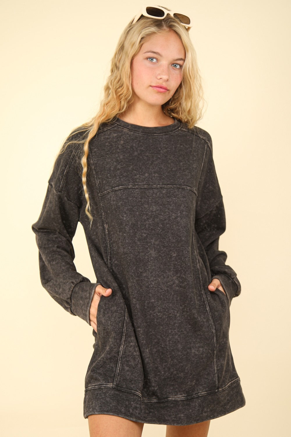 With long, wavy blond hair and sunglasses on their head, the person is wearing a VERY J Mineral Washed Oversized Sweatshirt Mini Dress with pockets against a beige background.