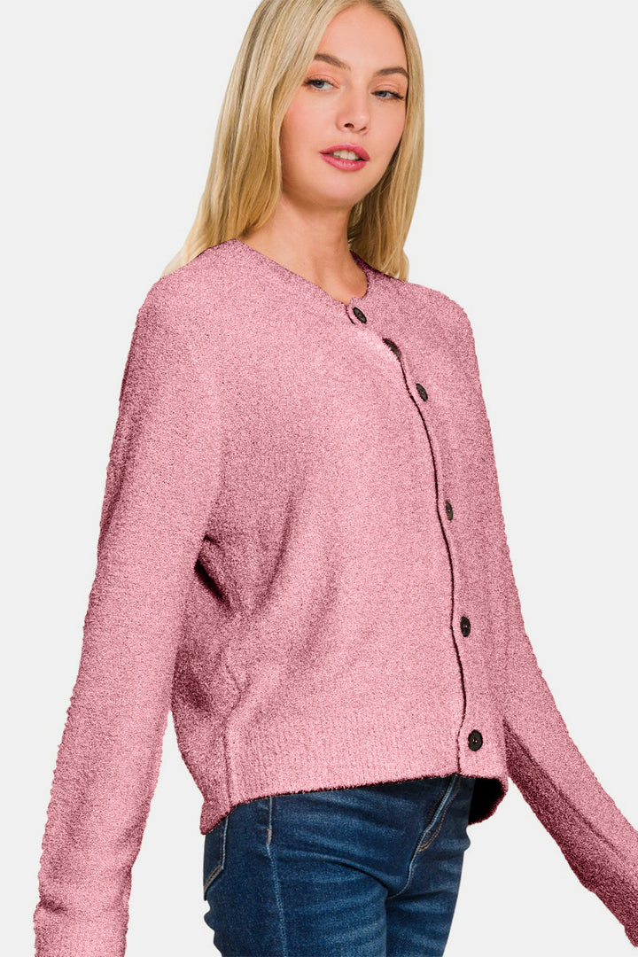 A person wearing the Zenana Button Down Long Sleeve Sweater Cardigan in pink, which features black buttons and a cozy textured knit design, stands against a plain background paired with blue jeans.